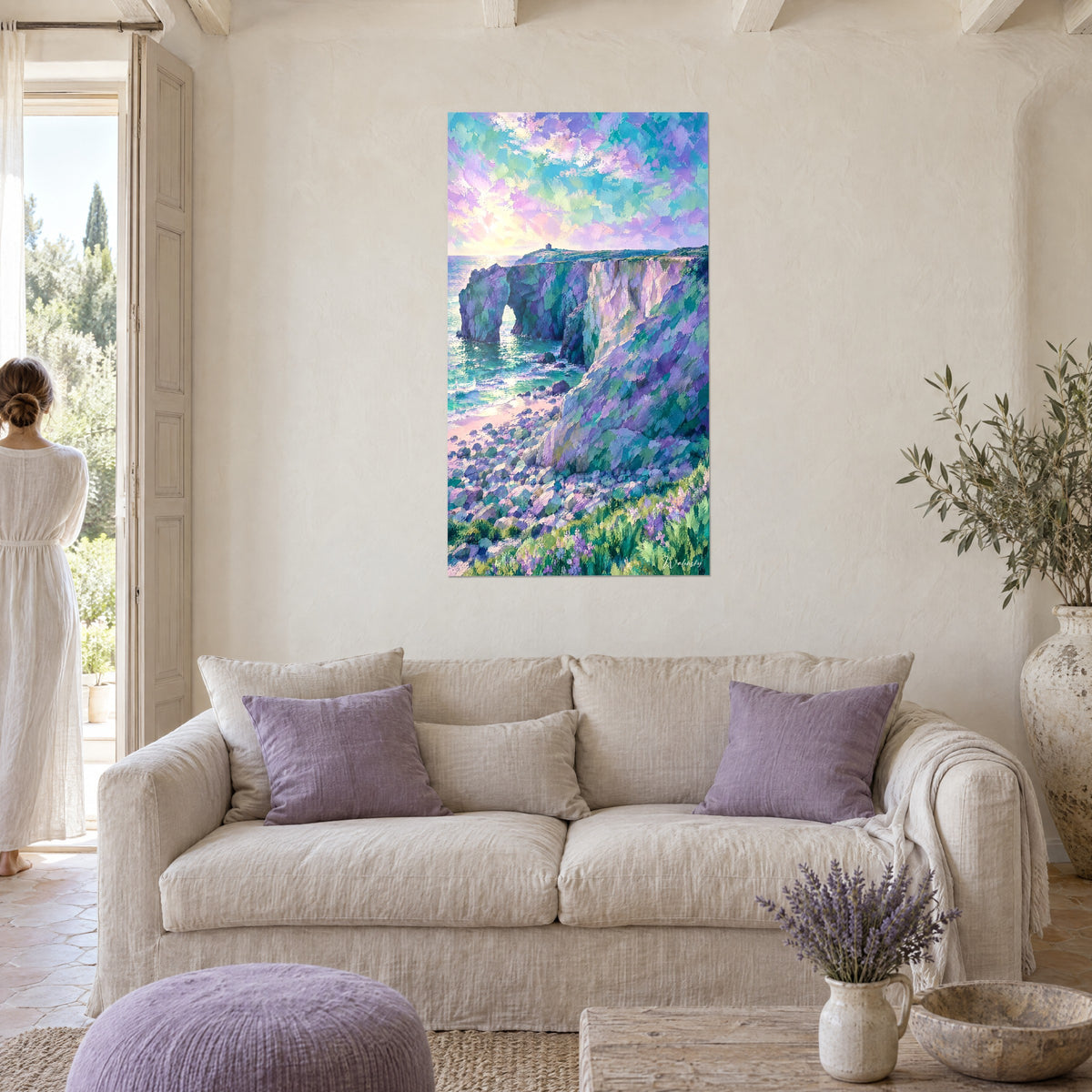 Gemälde Klippe in Violett mit einem Felsbogen, türkisfarbenes Meer und pastellfarbener Himmel, eine Frau von hinten über einem Sofa in einem hellen Wohnzimmer