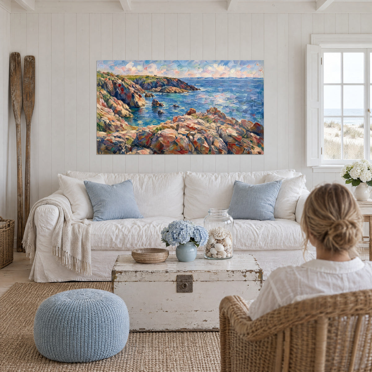 Cuadro de una cala bretona con rocas rosas y ocres, mar azul turquesa, encima de un sofá en un salón luminoso