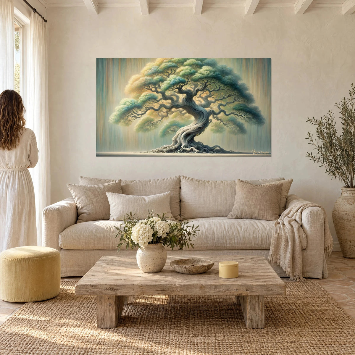Wall art tree of life with blue-green foliage and golden ochre canopy, pale twisted trunk, woman seen from behind, above a sofa in a bright living room