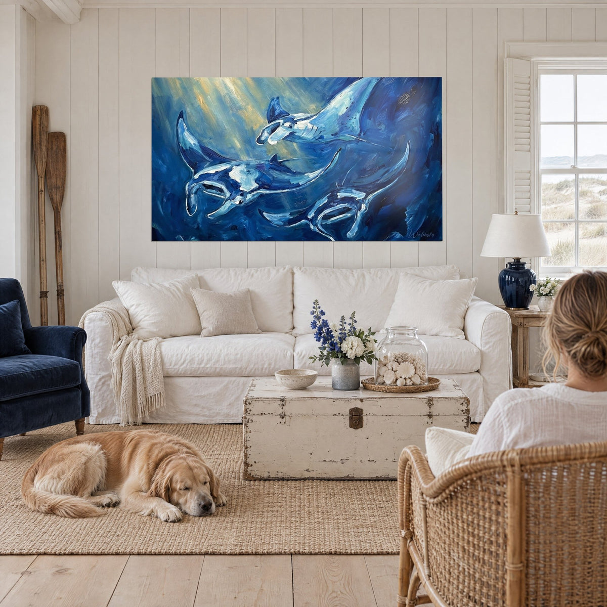 Wall art of manta rays in navy blue and pearly white beneath golden rays of light, above a sofa in a bright living room