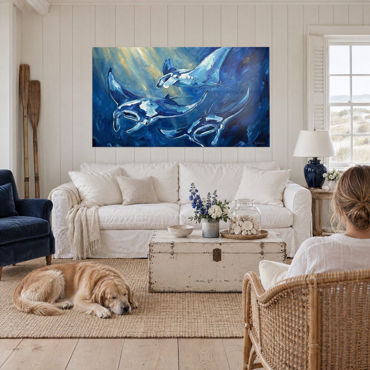 Tableau raies mantas bleu marine et blanc nacré sous des rais de lumière dorés, au-dessus d'un canapé dans un salon lumineux