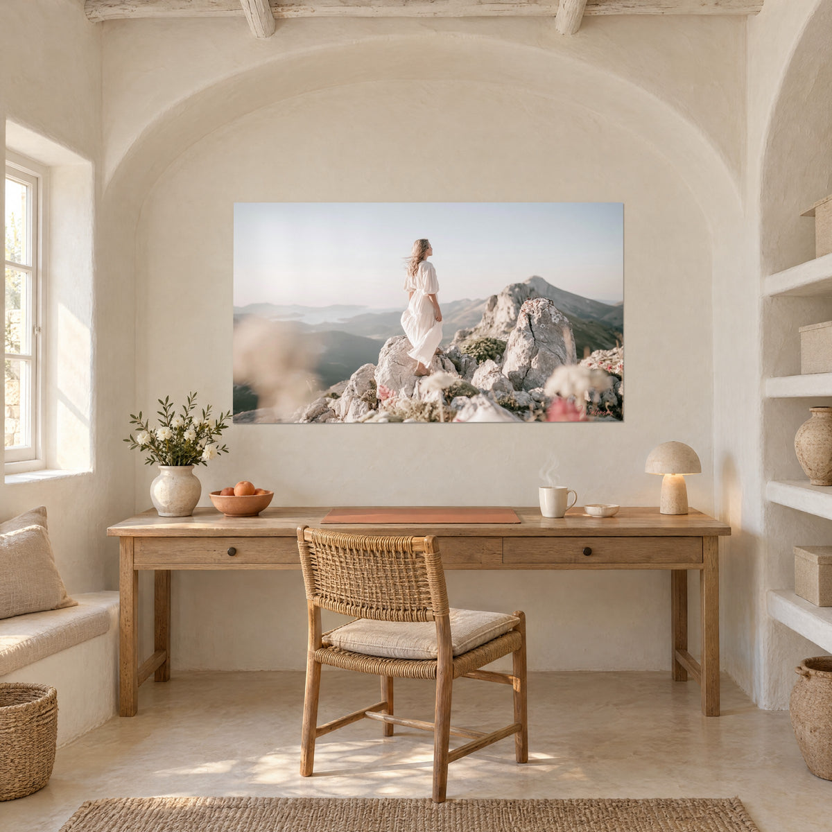 Wall art hiker in a white dress on pale rocks, blue-grey valleys and golden sky, wooden desk beneath a whitewashed arch