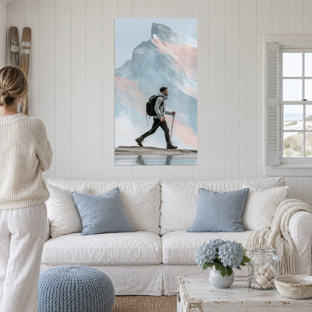 Tableau randonneur au sac noir marchant devant une montagne rose et bleue, au-dessus d'un canapé dans un salon lumineux