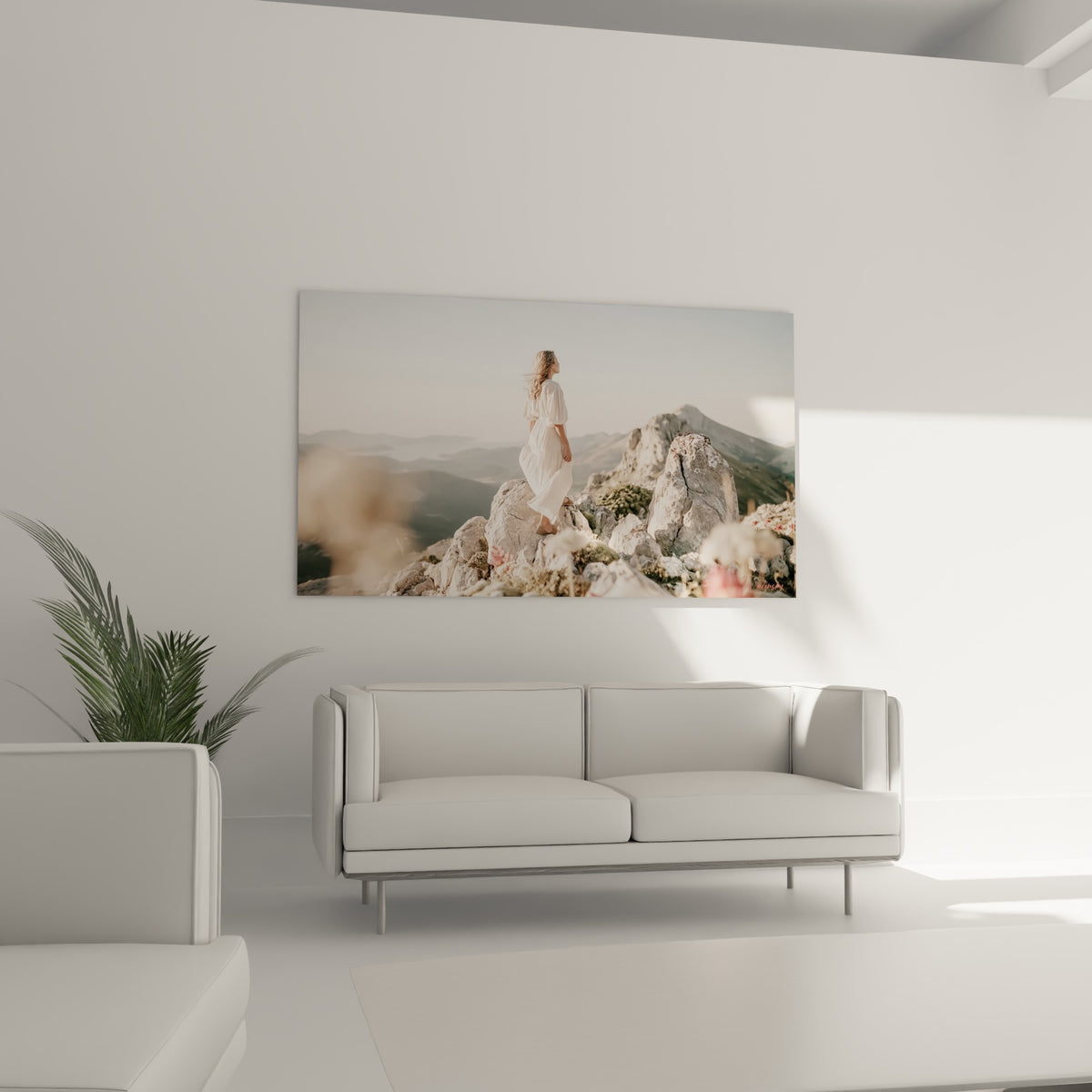 Femme en robe blanche contemplant les sommets gris et bleus, tableau au-dessus d'un canapé dans un salon lumineux