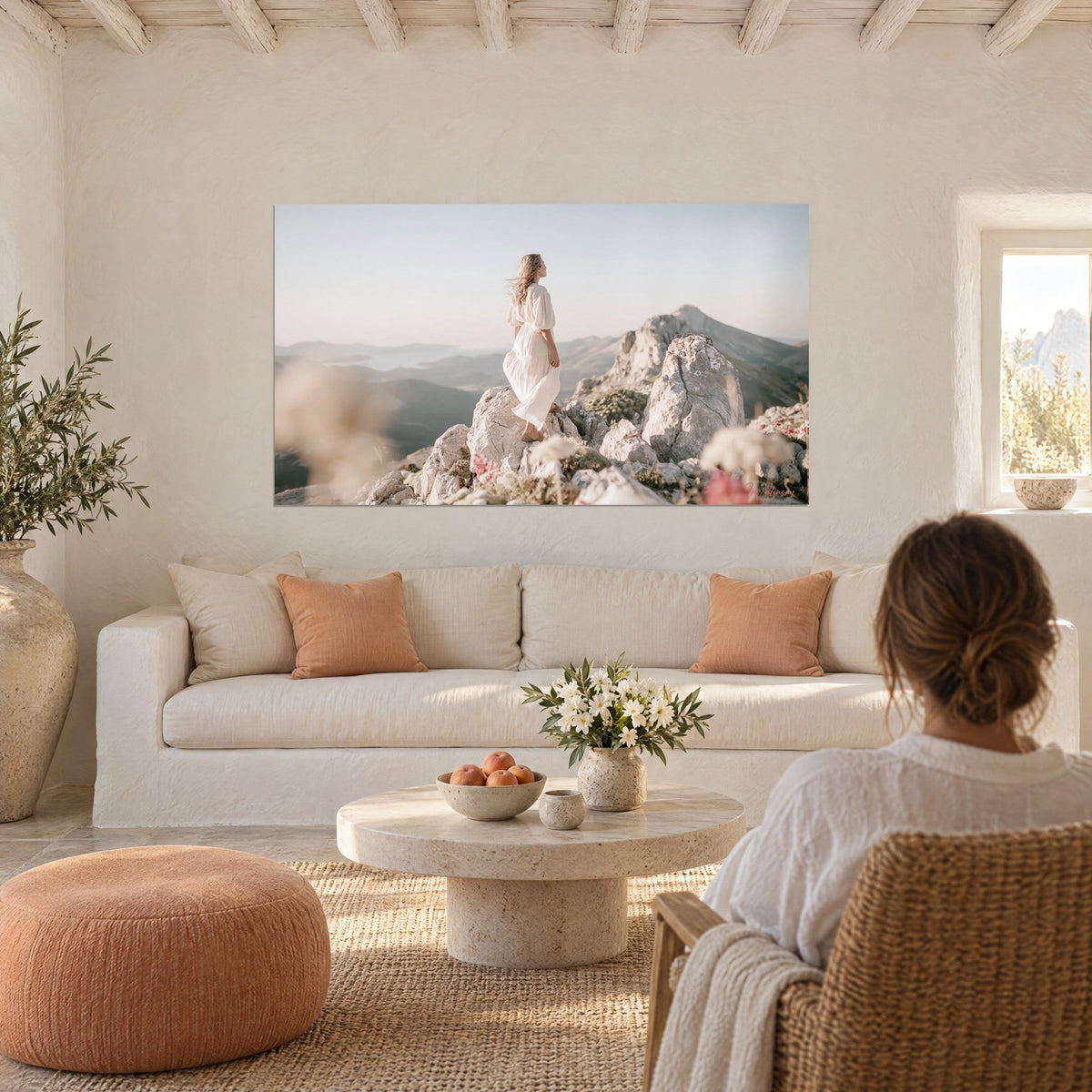 Tableau randonneuse en robe blanche sur un rocher, ciel pastel rosé et crêtes bleutées, au-dessus d'un canapé dans un salon lumineux