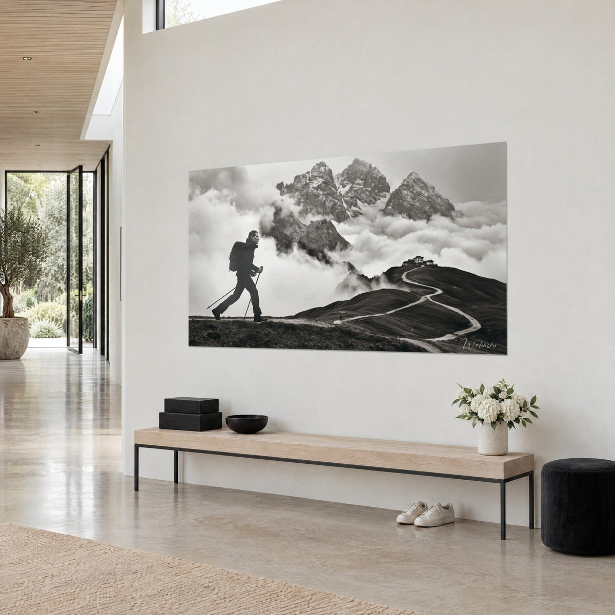 Tableau alpiniste de profil gravissant une crête, sentier pâle en lacets et refuge perché, noir et blanc, dans une maison d'architecte