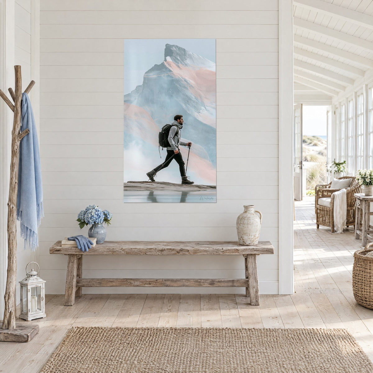 Tableau marcheur en pull gris et bâtons de trek, sommet pastel rose et bleu, sur un mur blanc de maison de bord de mer