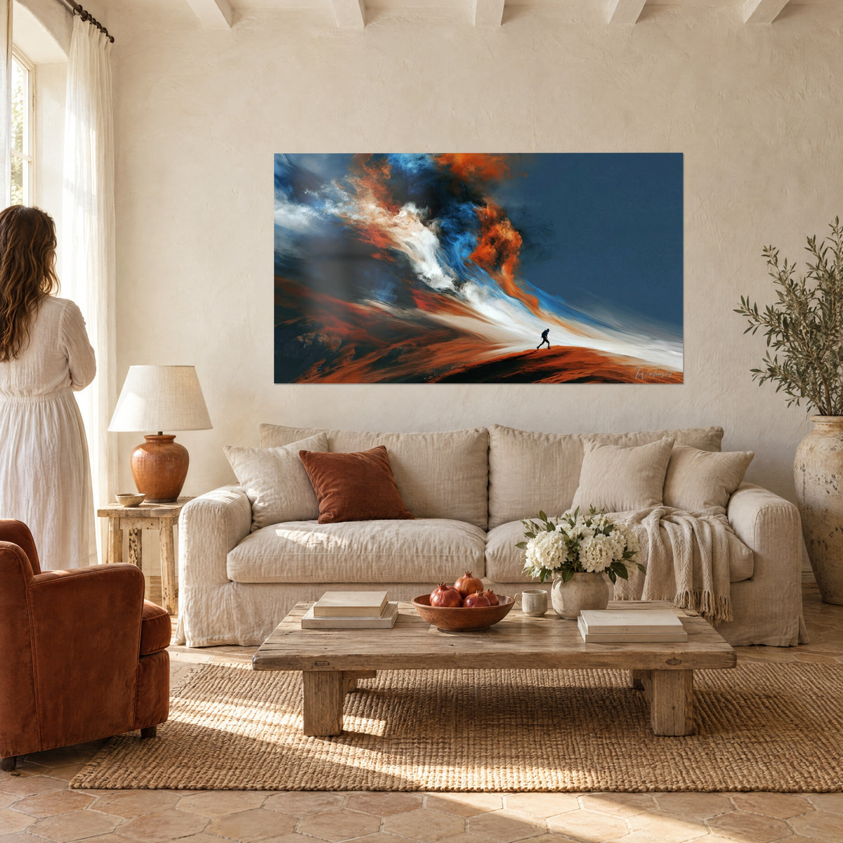 Wall art lone walker facing an orange and blue whirl, rust-coloured ridge, couple seen from behind above a sofa in a bright living room