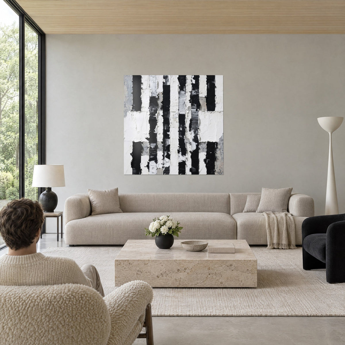 Quadro con strisce verticali nere su sfondo di intonaco imbiancato, una persona di spalle, sopra un divano in un soggiorno luminoso