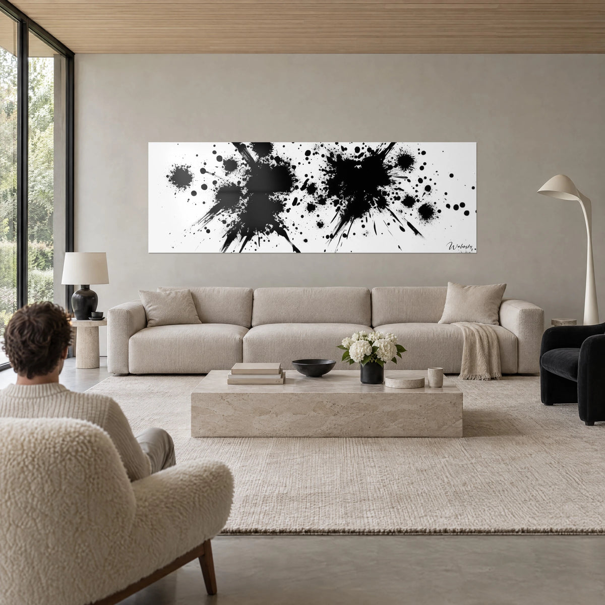 Wall art with black ink splashes bursting on a white background, two twin sprays, person seen from behind, above a sofa in a bright living room