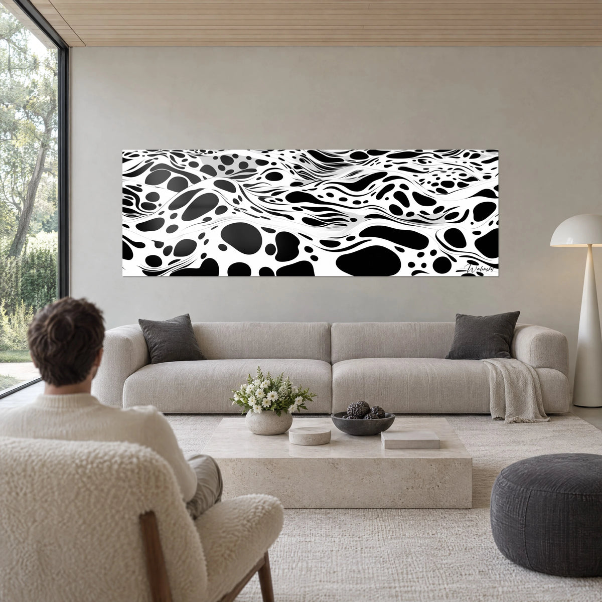 Quadro con motivo ondulato bianco e nero maculato, macchie ovali su fondo bianco, una persona di spalle, sopra un divano in un soggiorno luminoso