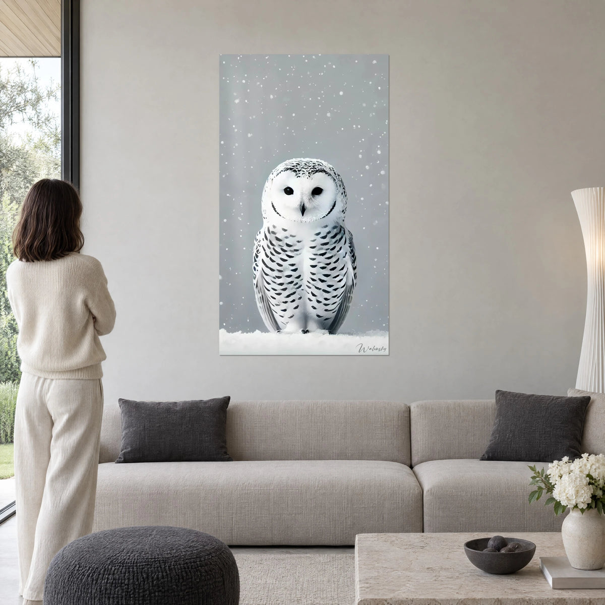 Schilderij sneeuwuil met zwarte vlekjes op een besneeuwde grijze achtergrond, boven een bank in een lichte woonkamer