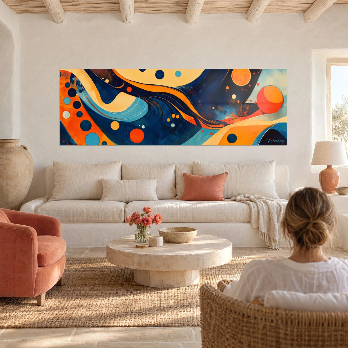 Tableau cercles orange et bleu nuit sur vagues abstraites dorées, femme de dos, au-dessus d'un canapé dans un salon lumineux