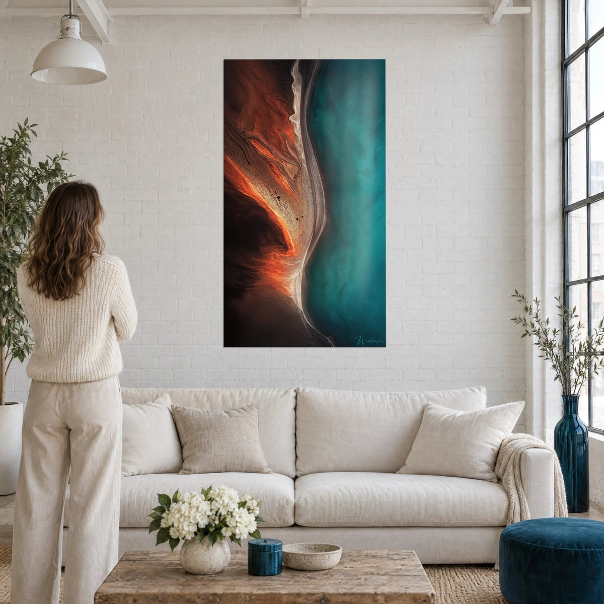 Schilderij kustlijn vanuit de lucht, oranje lava en turquoise zee, vrouw van achteren, boven een bank in een lichte woonkamer
