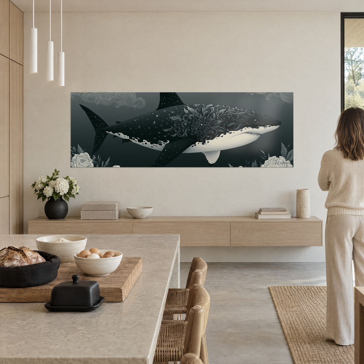 Tableau grand requin gravé de feuillages argentés sur fond gris-vert profond, cuisine ouverte, femme beige de dos devant l'œuvre