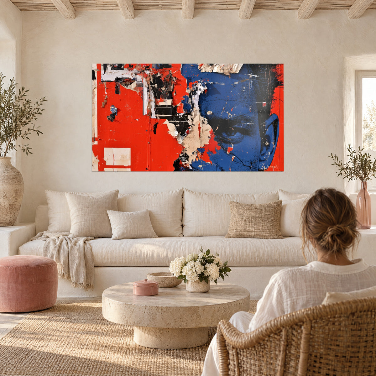 Cuadro de un rostro azul cobalto que emerge de un cartel rojo vivo rasgado, sobre un sofá en un salón luminoso
