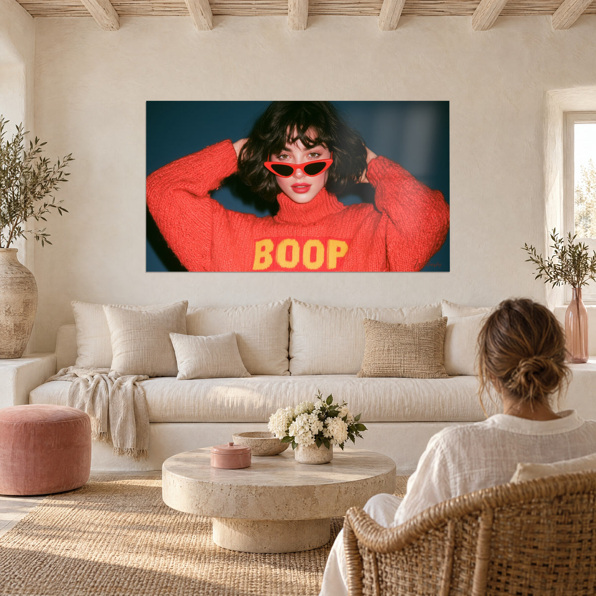 Wall art of a young brunette woman in red glasses, coral BOOP sweater with yellow lettering, midnight blue background, above a sofa in a bright living room