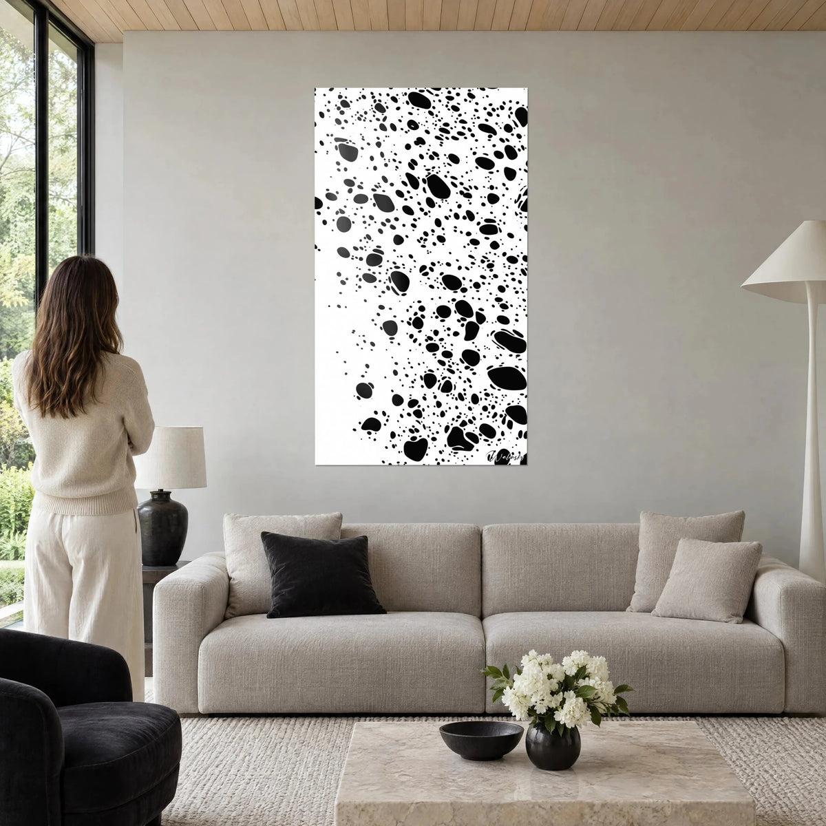Wall art with black ink splashes on pure white background, woman seen from behind, above a sofa in a bright living room