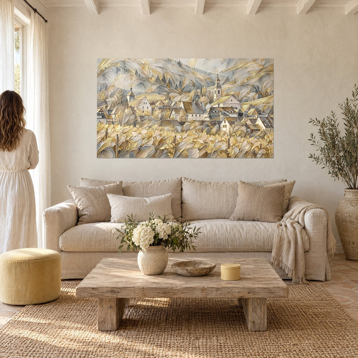 Cuadro pueblo alsaciano de tejados dorados y viñedos frondosos en beige y oro, mujer de espaldas, encima de un sofá en un salón luminoso