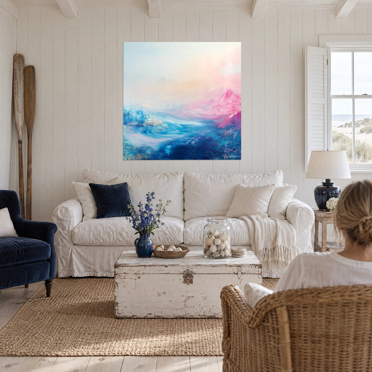Wall art abstract pink and blue landscape, impasto waves under a cream sky, hanging above a sofa in a bright living room