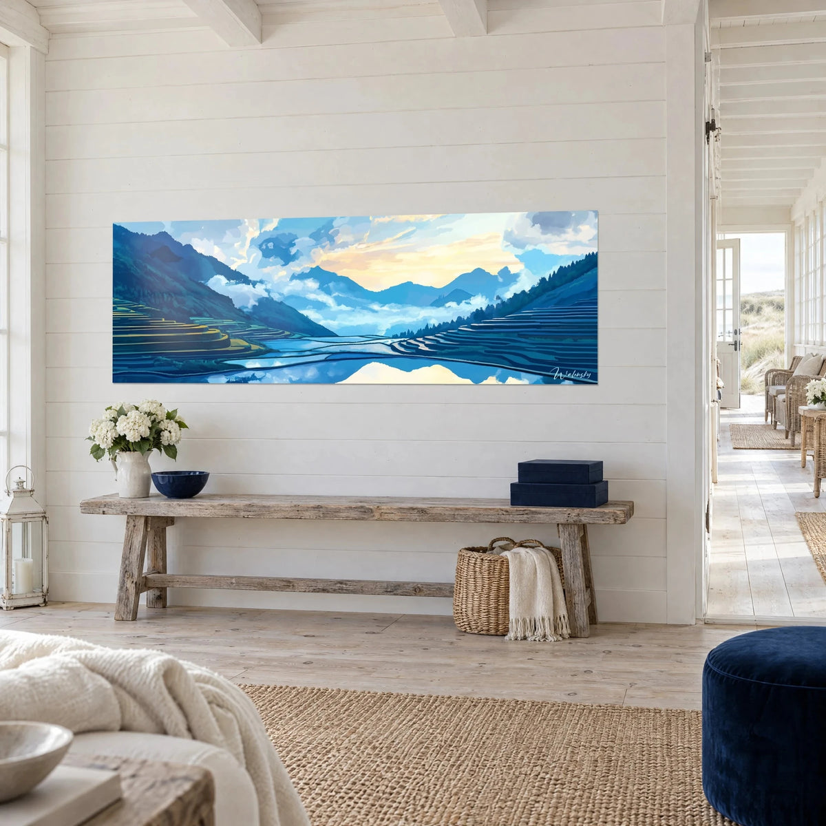 Tableau paysage de montagne bleu et ocre, mer de nuages et eau reflétant le ciel, sur un mur blanc lambrissé près d'une console