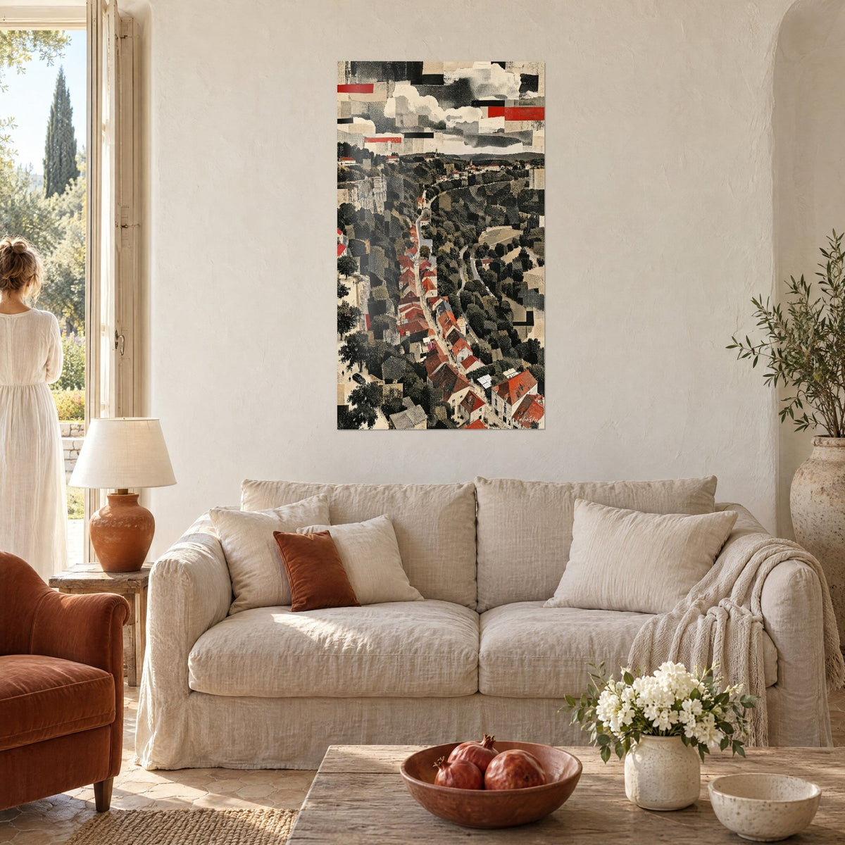 Wall art of a hilltop village with red rooftops in collage seen from above, grey cliff and clouds, couple seen from behind above a sofa in a bright living room