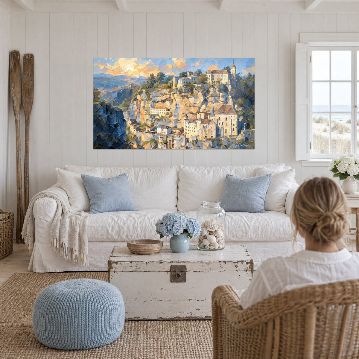 Quadro villaggio di pietra aggrappato alla rupe, ocra e blu, cielo dorato, sopra un divano in un soggiorno luminoso