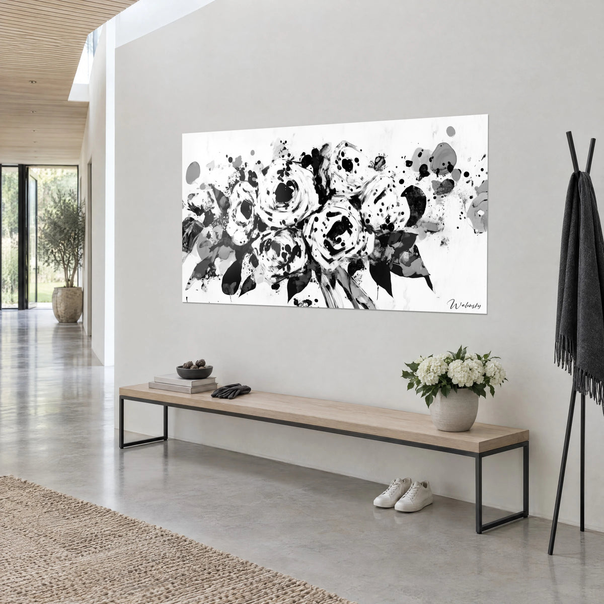 Cuadro flores de tinta con pétalos espiralados en negro y blanco, gotas dispersas, colgado en diagonal junto a un banco de madera clara
