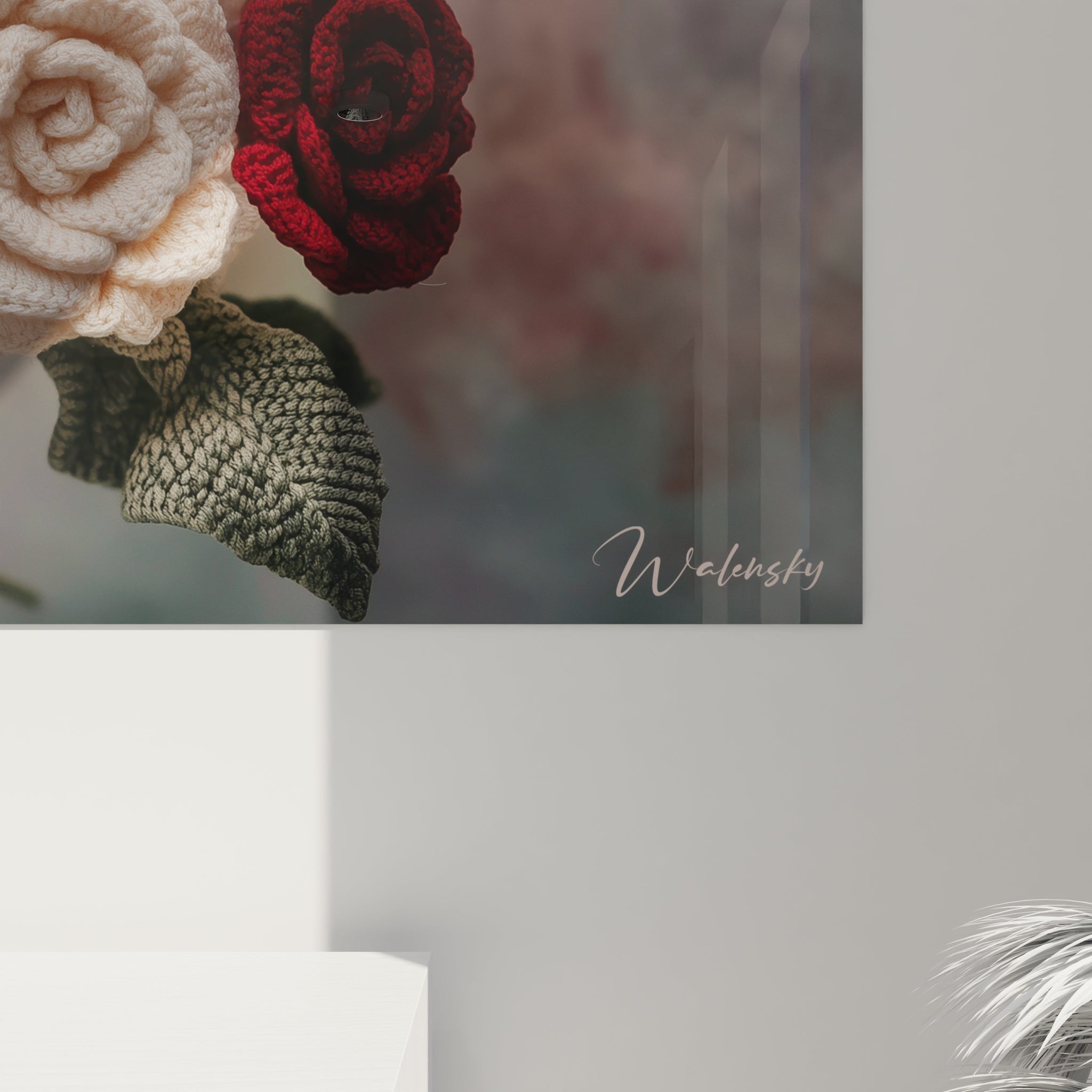 Un tableau crochet floral exhibant un assemblage serré de roses tricotées en fil rouge, blanc et rose pâle, chaque fleur présentant des détails minutieux de pétales superposés et des feuilles vertes texturées, formant une composition équilibrée et raffinée.
