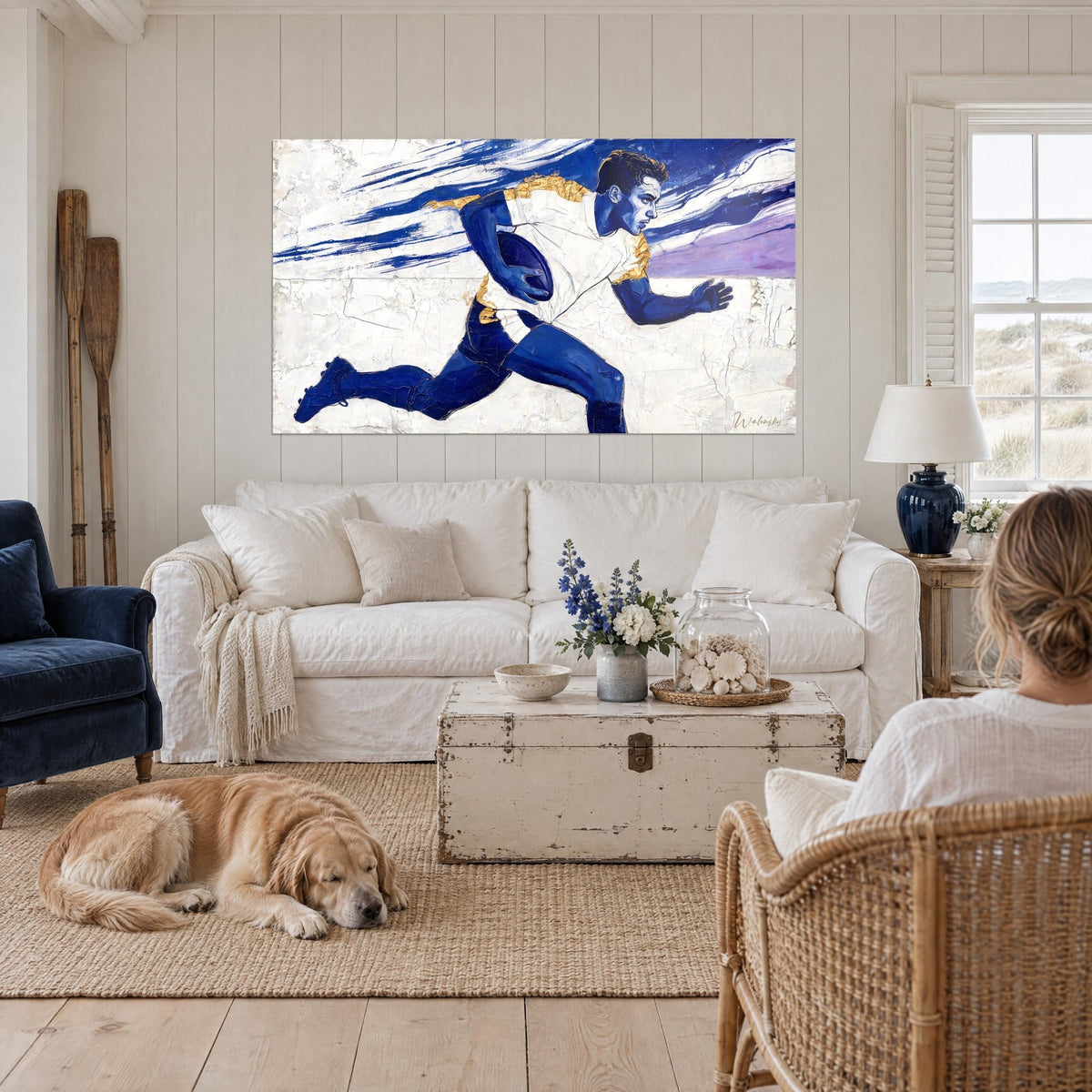 Tableau rugbyman bleu cobalt en pleine course, ballon sous le bras, maillot blanc rehaussé d'or, au-dessus d'un canapé dans un salon lumineux