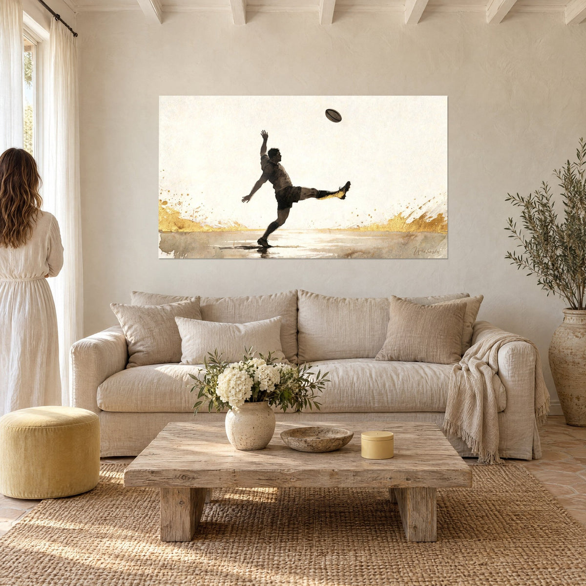 Tableau botteur de rugby en plein coup de pied, maillot brun, éclaboussures dorées, vu de dos par une femme au-dessus d'un canapé dans un salon lumineux