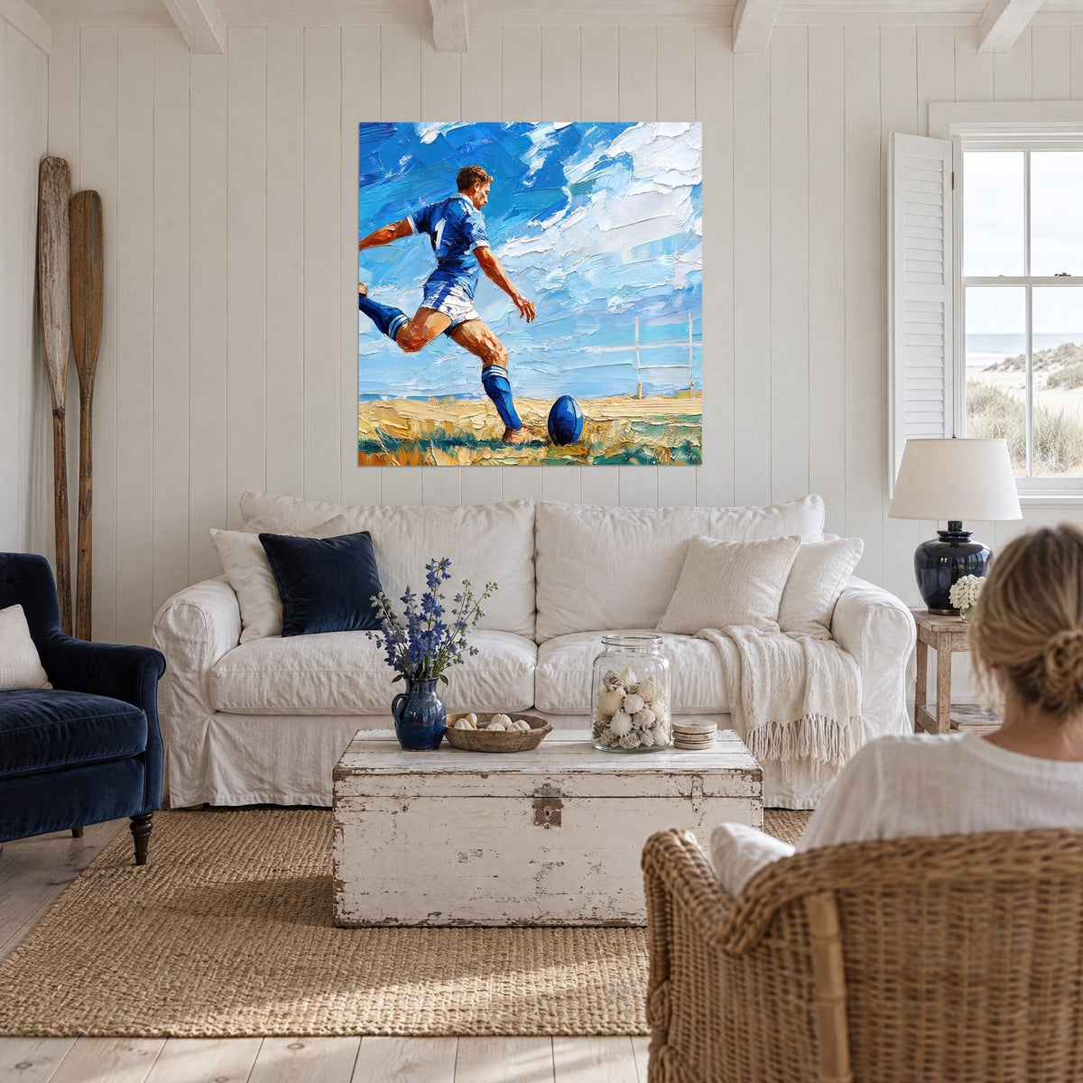 Tableau rugbyman en maillot bleu et blanc armant sa frappe, ciel azur empâté, au-dessus d'un canapé dans un salon lumineux