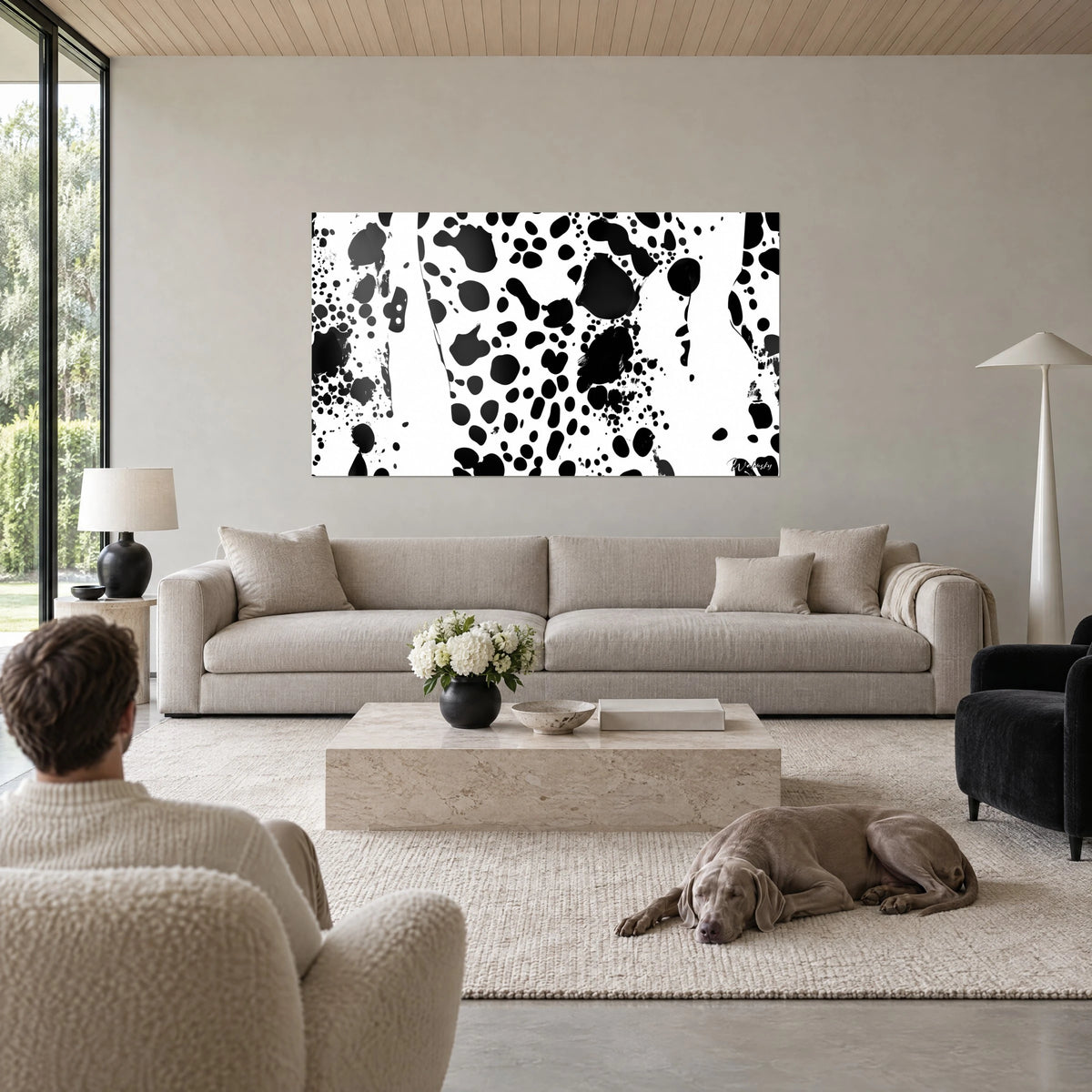 Cuadro con salpicaduras de tinta negra sobre fondo blanco, hombre de espaldas y un Weimaraner tumbado, encima de un sofá en un salón luminoso