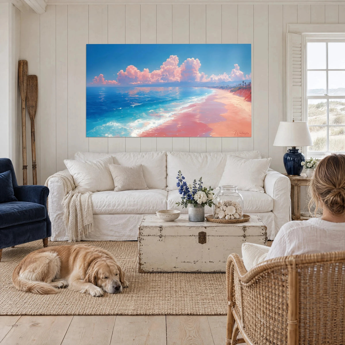 Quadro di spiaggia di sabbia rosa orlata di schiuma bianca e acqua turchese, nuvole rosa, appeso sopra un divano in un soggiorno luminoso