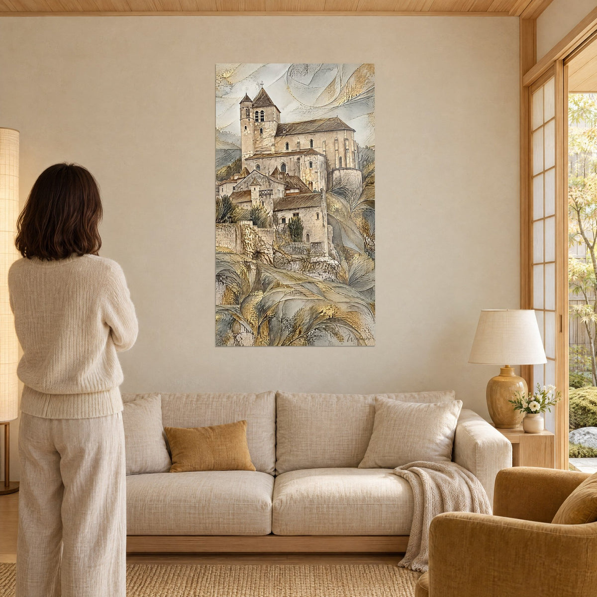 Wall art church perched on beige stone cliff, square bell tower, golden and grey rocks, woman seen from behind above a sofa in a bright living room
