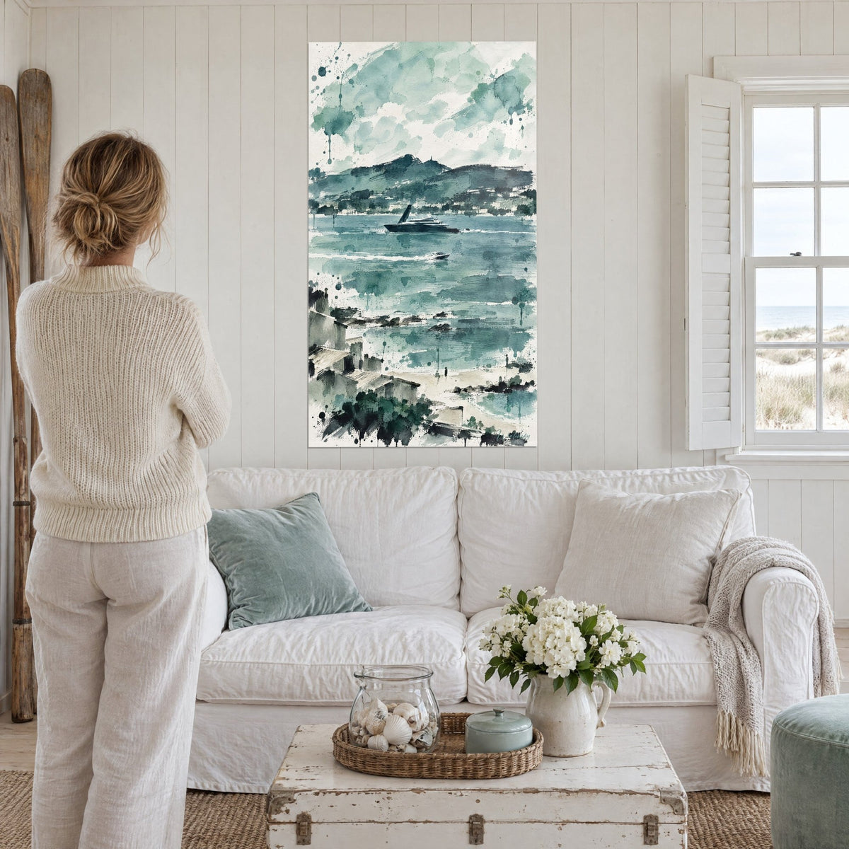 Gemälde mit dunkler Yacht auf türkisfarbener Bucht, aquarellierte graugrüne Hügel, über einem Sofa in einem hellen Wohnzimmer