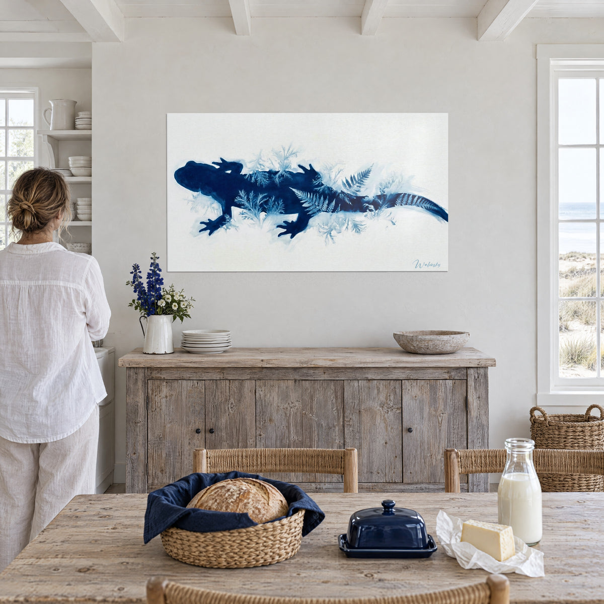 Cuadro tritón en cianotipo azul profundo salpicado de hojas de helecho pálidas sobre fondo crema, frente a una mesa de madera en una cocina marinera