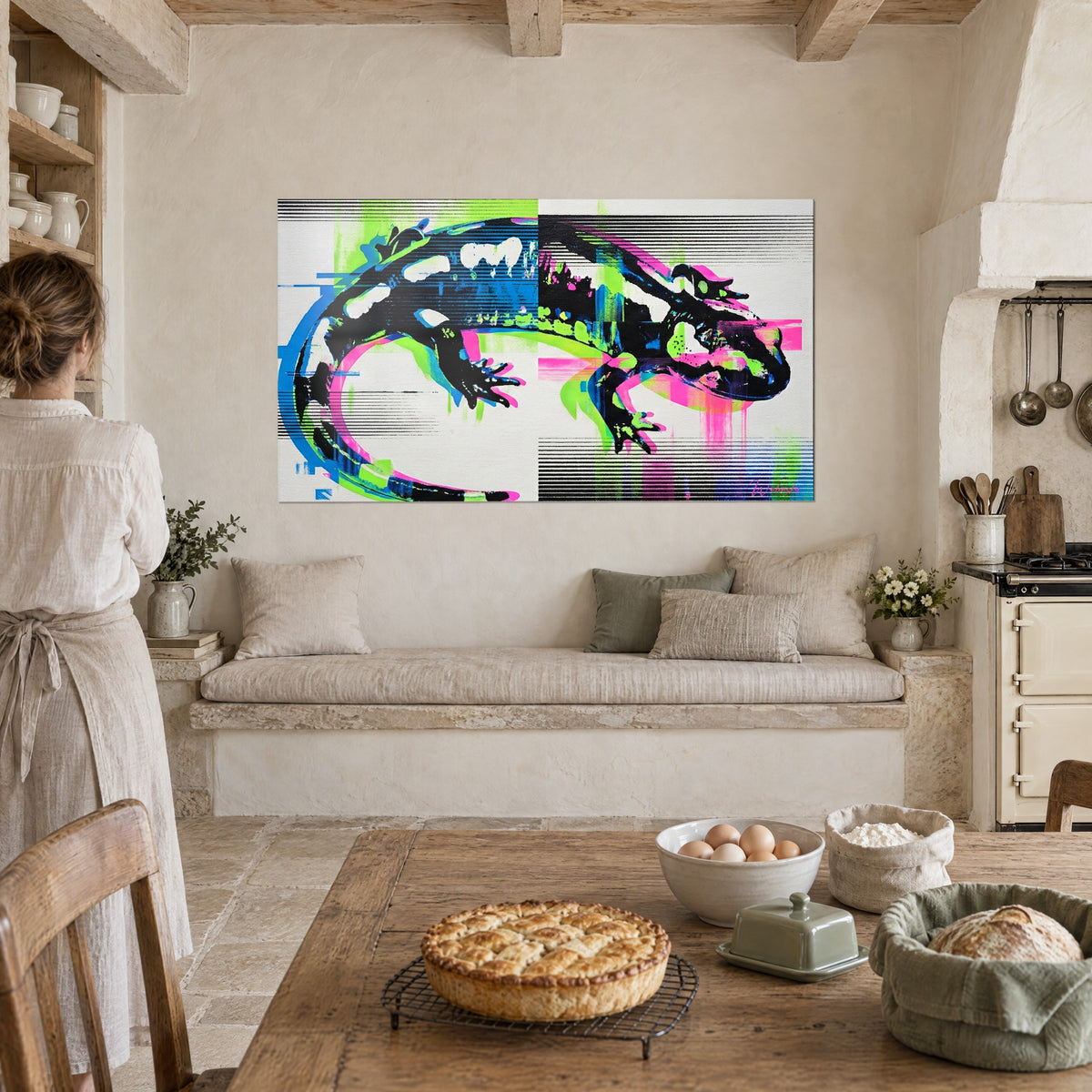 Wall art black newt with webbed feet, neon green and magenta offsets, a woman seen from behind beside a tart in a stone kitchen