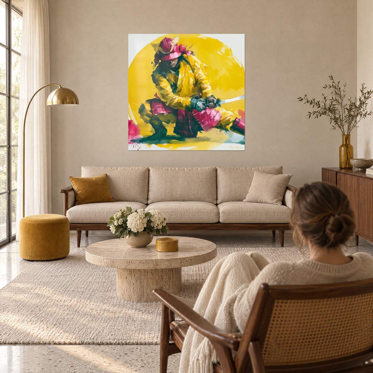 Πίνακας γονατιστού πολεμιστή σε κίτρινο κερωμένο ύφασμα και ροζ κράνος, με σπαθί στο χέρι, μια γυναίκα από πίσω, πάνω από καναπέ σε φωτεινό σαλόνι