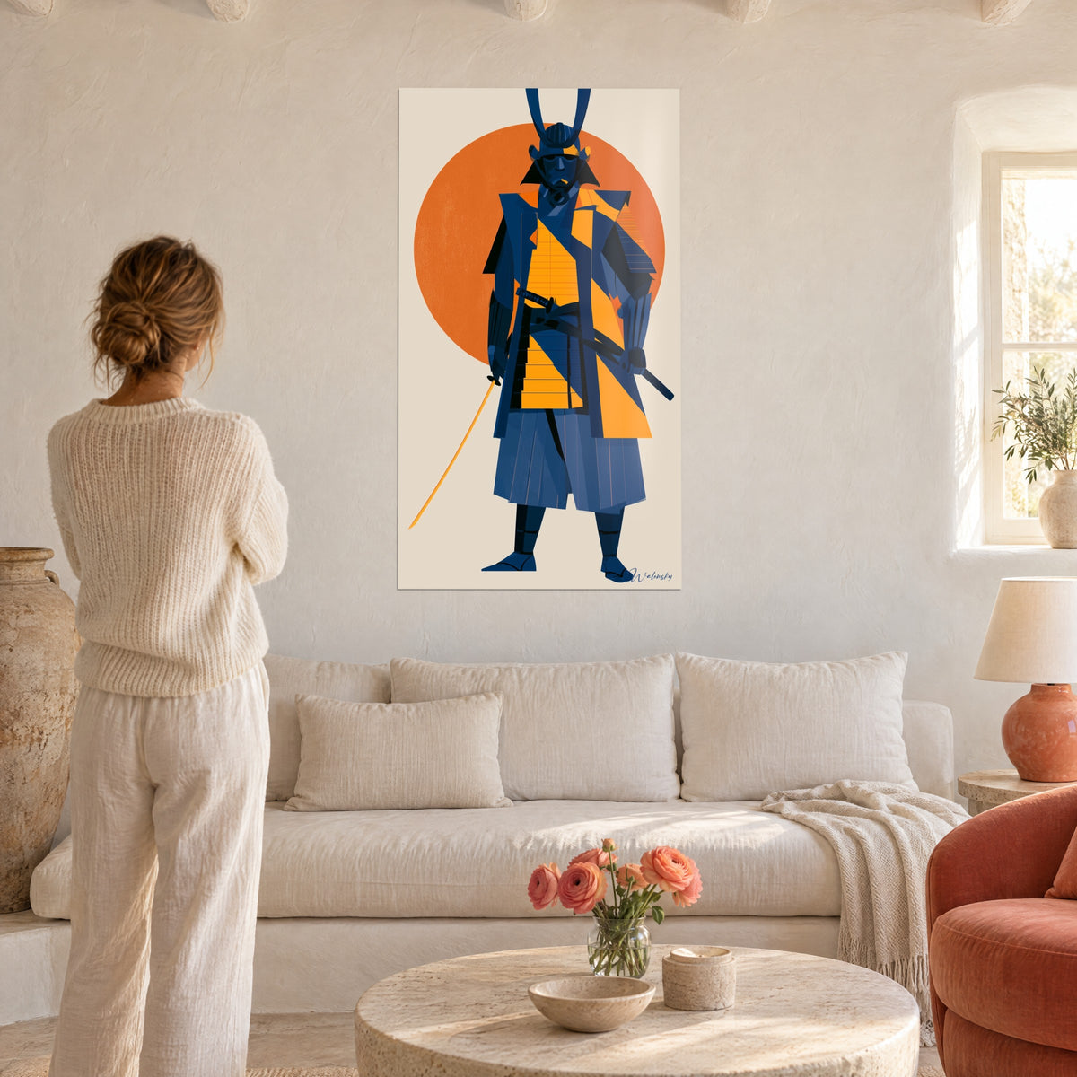 Tableau samouraï bleu marine à plastron orange, soleil rouge derrière lui, femme de dos au-dessus d'un canapé dans un salon lumineux