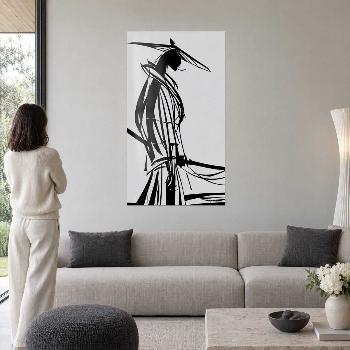 Tableau samouraï filiforme au large chapeau conique, silhouette noire sur fond gris clair, au-dessus d'un canapé dans un salon lumineux