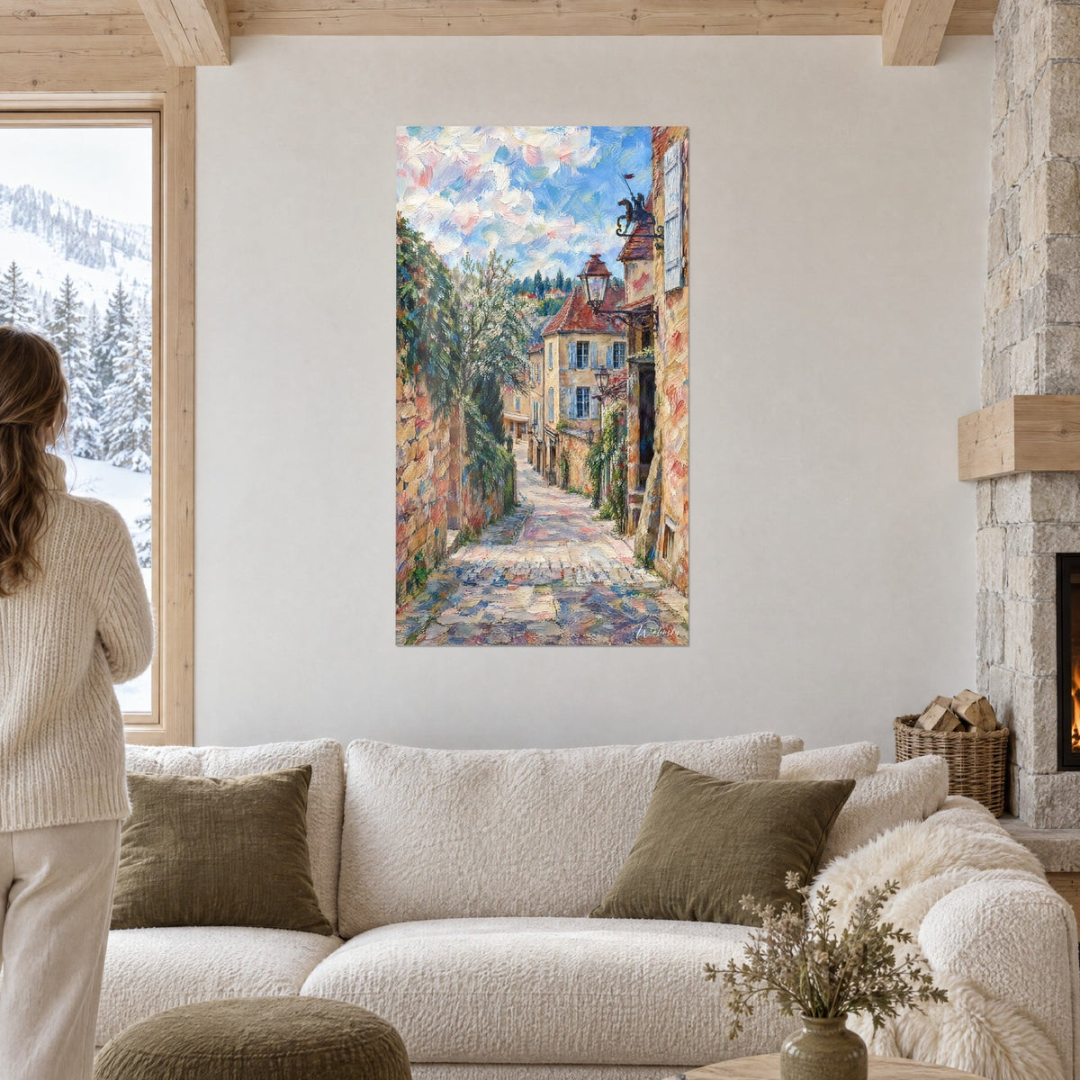 Schilderij van een keienstraatje met okerkleurige stenen en terracotta daken, blauwe lucht met roze vlekjes, boven een bank in een lichte woonkamer