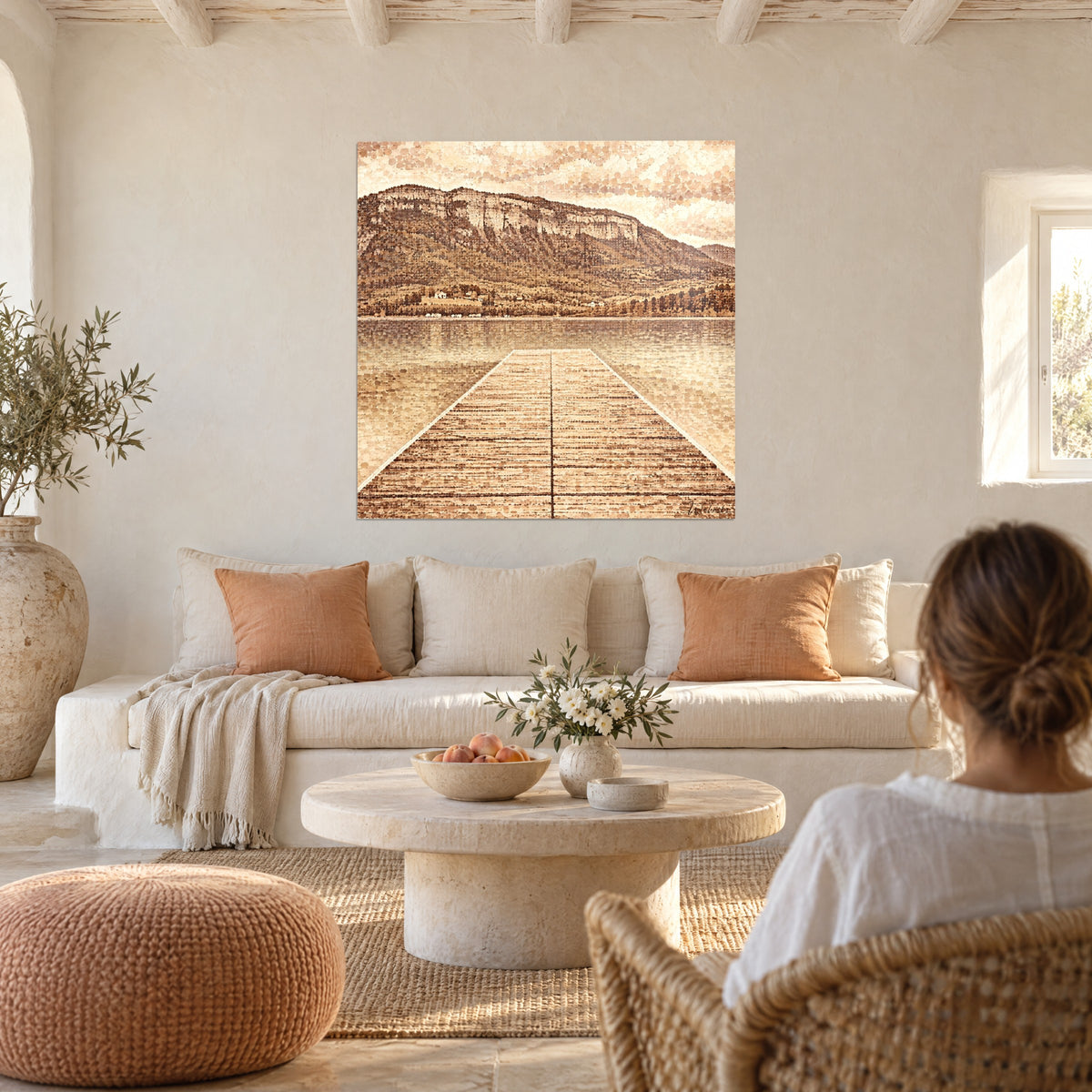 Cuadro muelle de madera que se adentra en un lago sepia hacia su acantilado, caramelo y crema, encima de un sofá en un salón luminoso