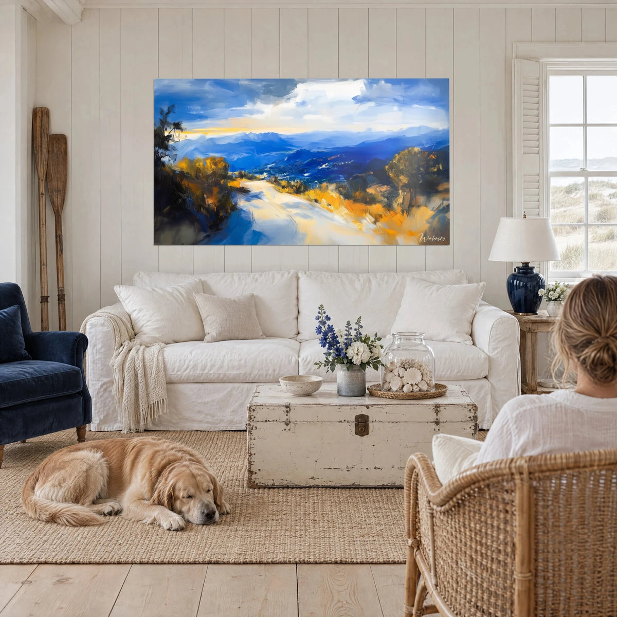 Quadro sentiero luminoso che serpeggia verso montagne blu cobalto, fogliame ocra, sopra un divano in un soggiorno illuminato dal sole