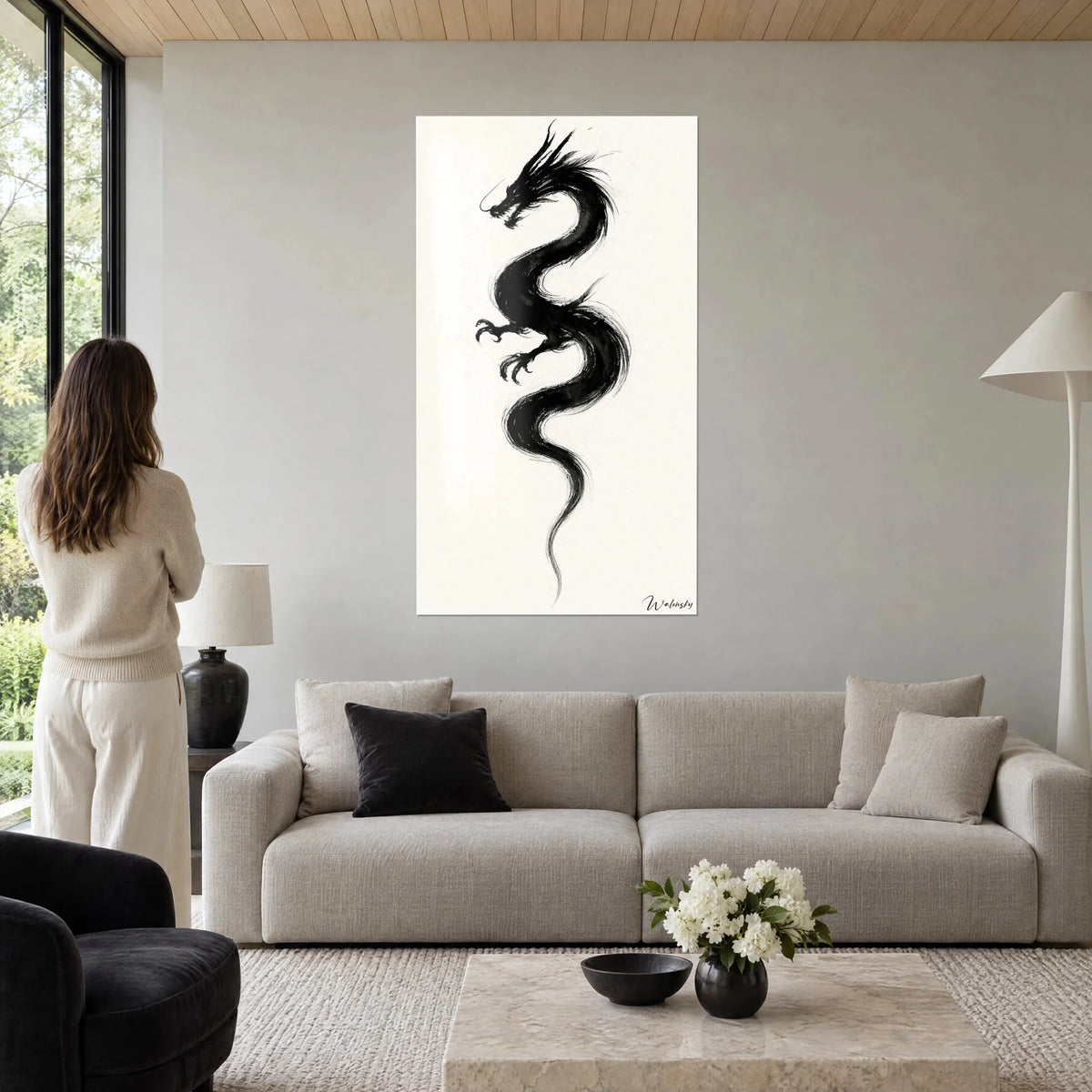 Quadro drago cinese in inchiostro nero con artigli distesi su fondo crema, donna di schiena, sopra un divano in un soggiorno luminoso