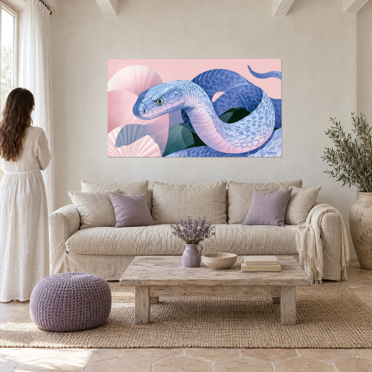Wall art of a lavender-blue snake coiled on a powder-pink background, green eye, woman seen from behind above a sofa in a bright living room