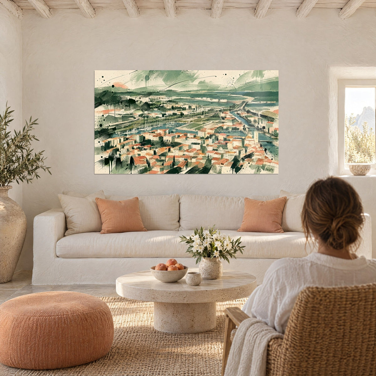 Gemälde Panorama von Sète mit terrakottafarbenen Dächern und salbeigrünem Kanal, eine Frau von hinten über einem Sofa in einem hellen Wohnzimmer