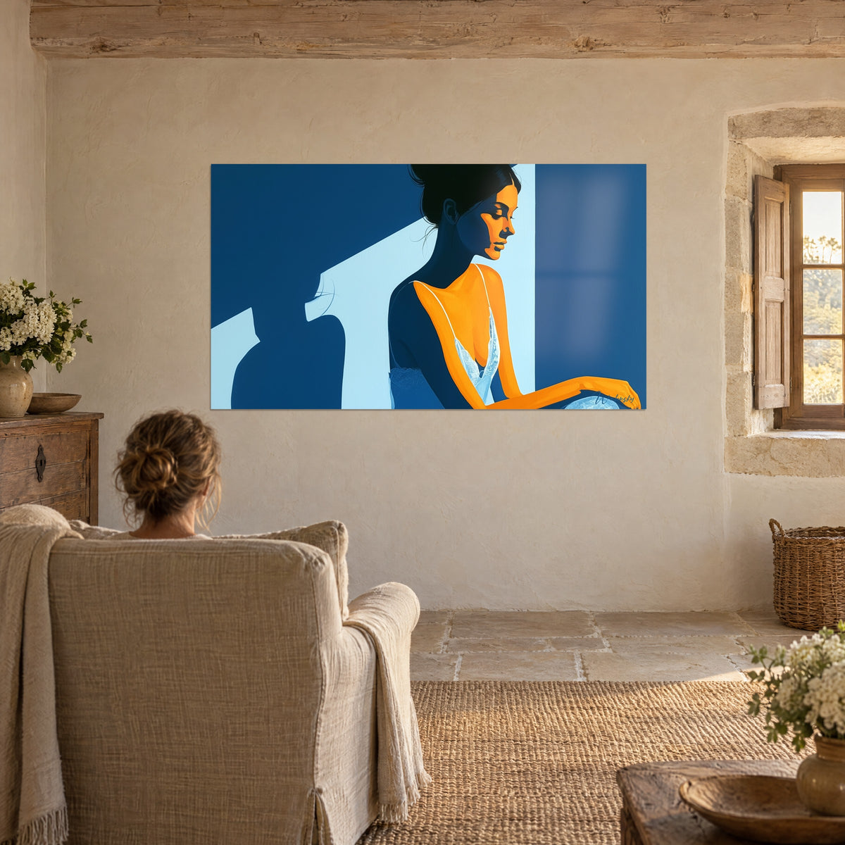 Tableau dormeuse éveillée au profil doré, aplats bleu roi et bleu ciel, accroché face à un fauteuil beige dans un salon en pierre