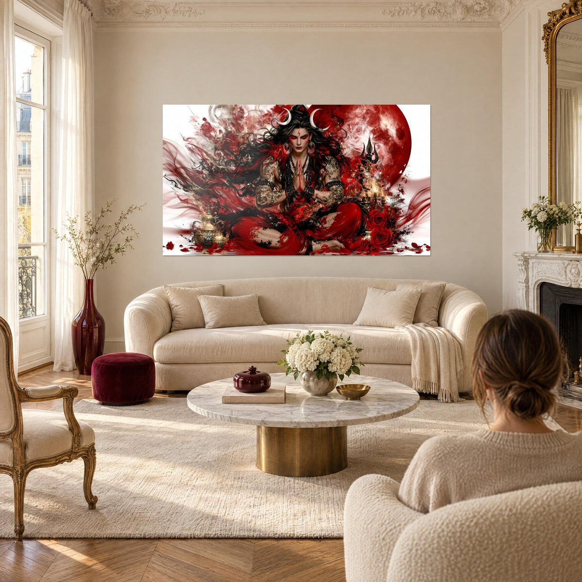 Wall art of a deity with crescent moons and joined hands, blood red and black, above a sofa in a bright living room