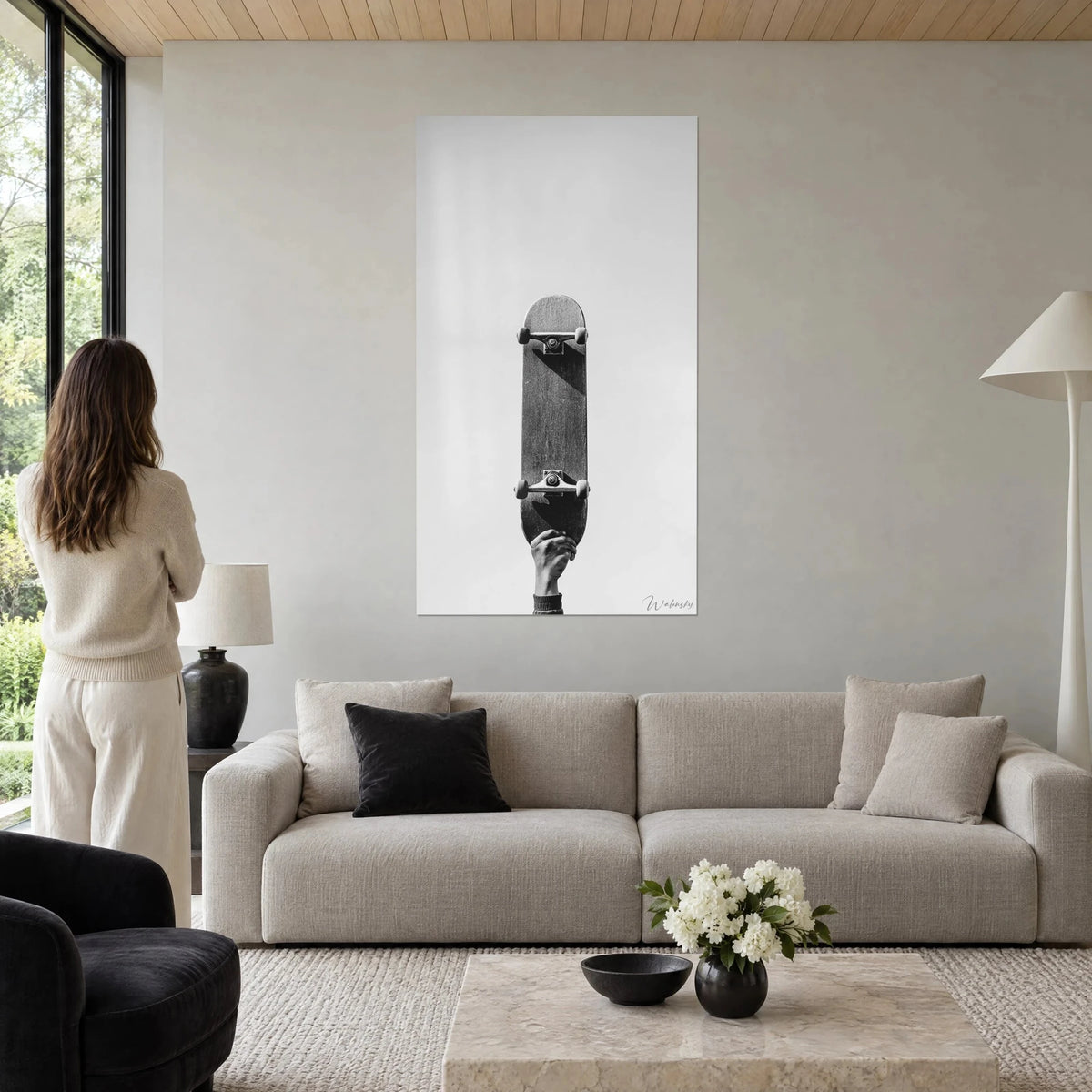 Tableau skateboard dressé vers le ciel, main levée, gris argenté et noir profond, femme de dos, au-dessus d'un canapé dans un salon lumineux